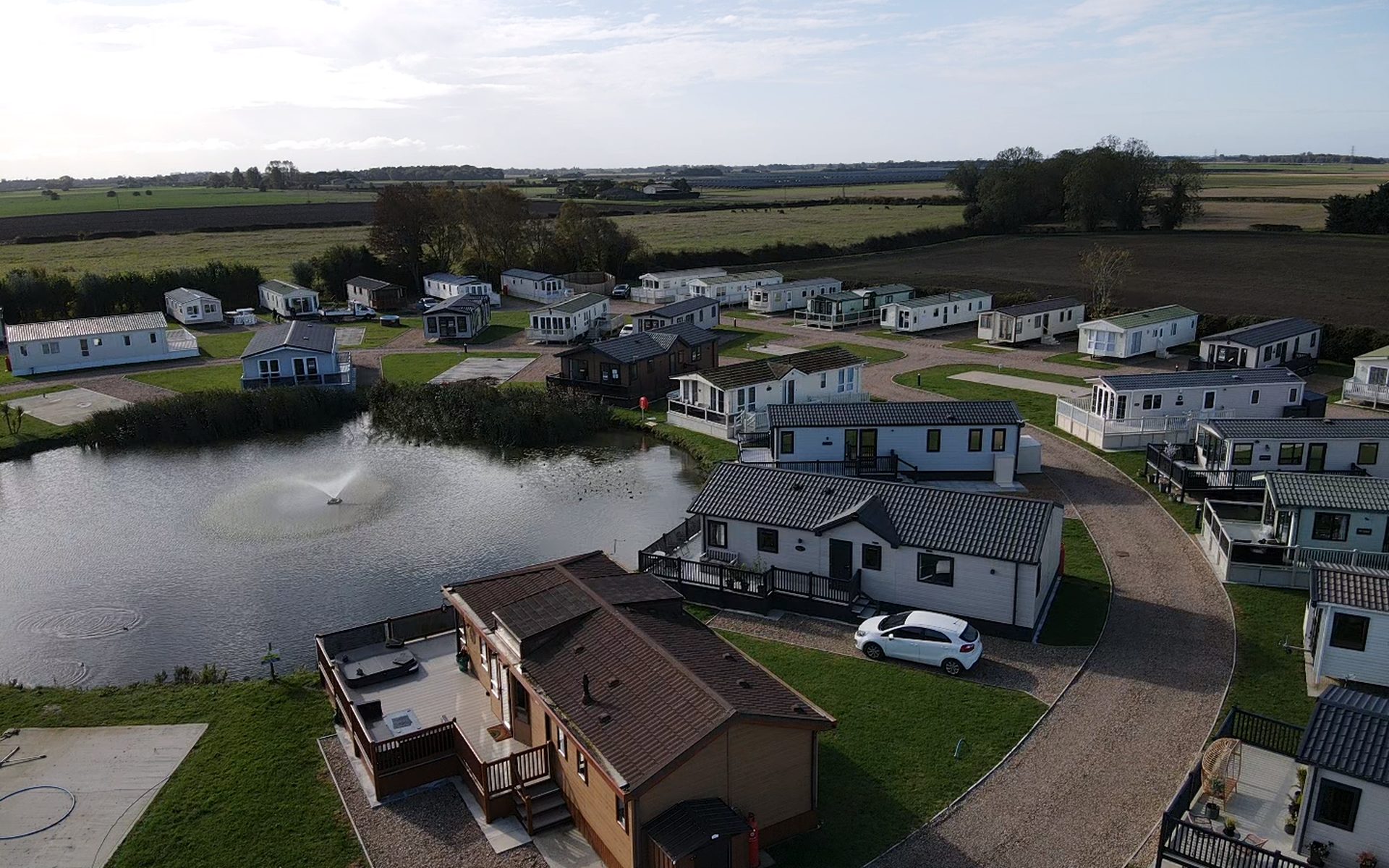 Aerial view of Barkham Manor holiday park, showing lodges and static caravans set around the central fishing lake and its fountain, with open Lincolnshire farmland beyond