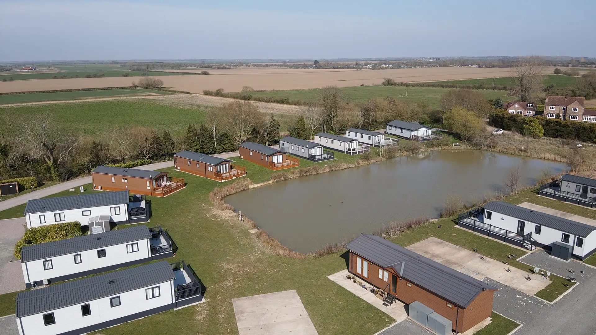 Aerial view of Faulkers Lakes Holiday Park, with timber-clad lodges and static caravans arranged around the fishing lake and open Lincolnshire farmland beyond